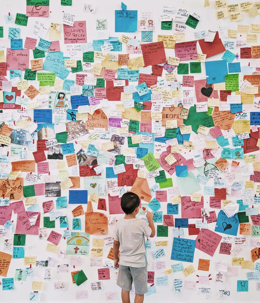 A child stands before a wall covered with colorful notes and messages, exploring creativity and expression.